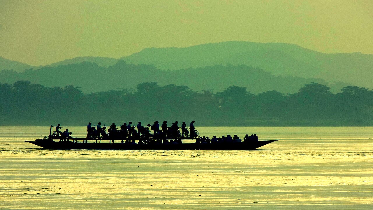 A crowded ferry carrying people and bicycles across the Brahmaputra in the evening